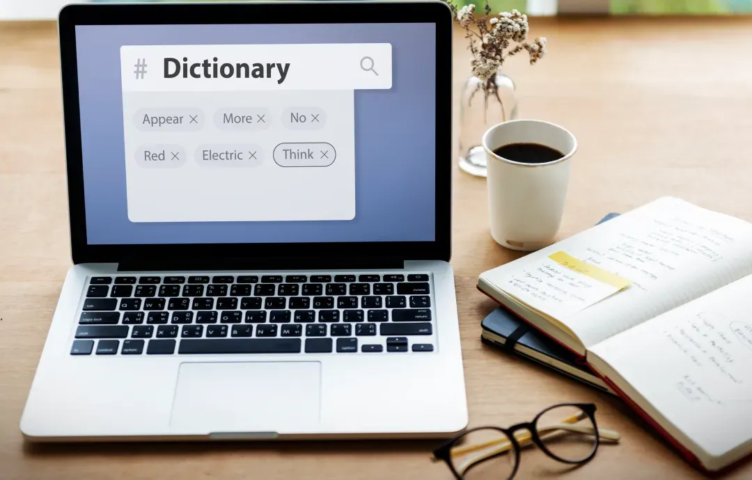A laptop displaying a digital dictionary interface on a desk next to an open notebook