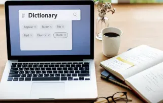 Ein Laptop mit einem digitalen Wörterbuch auf einem Schreibtisch neben einem offenen Notizbuch
