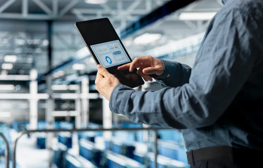 A worker checking a data dashboard on a tablet inside a modern factory