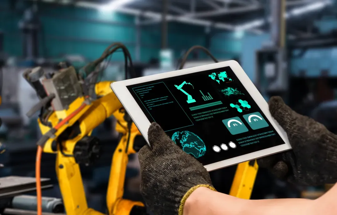A factory worker using a tablet to monitor machine data in front of a yellow robotic arm