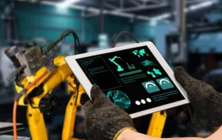 Ein Fabrikarbeiter überwacht Maschinendaten auf einem Tablet vor einem gelben Roboterarm