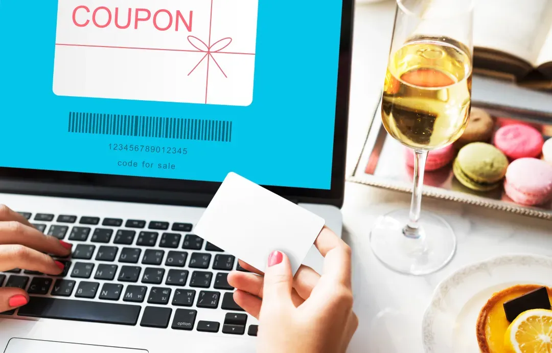 A person holding a card while looking at a digital coupon on a laptop screen