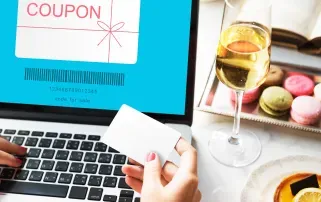 Eine Person hält eine Karte und betrachtet einen digitalen Gutschein auf einem Laptop-Bildschirm